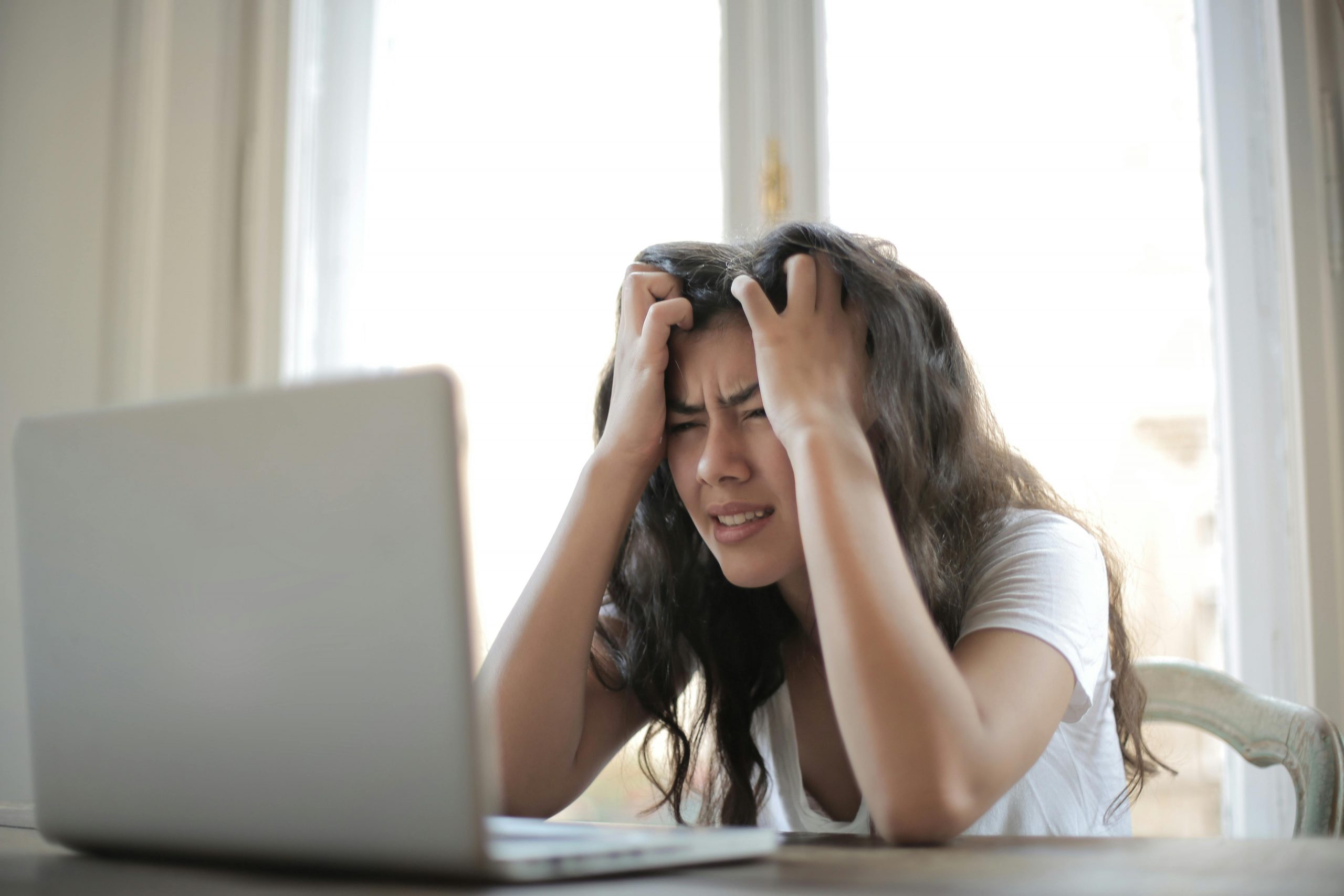 stressed woman pulling her hair while sitting in front of a laptop