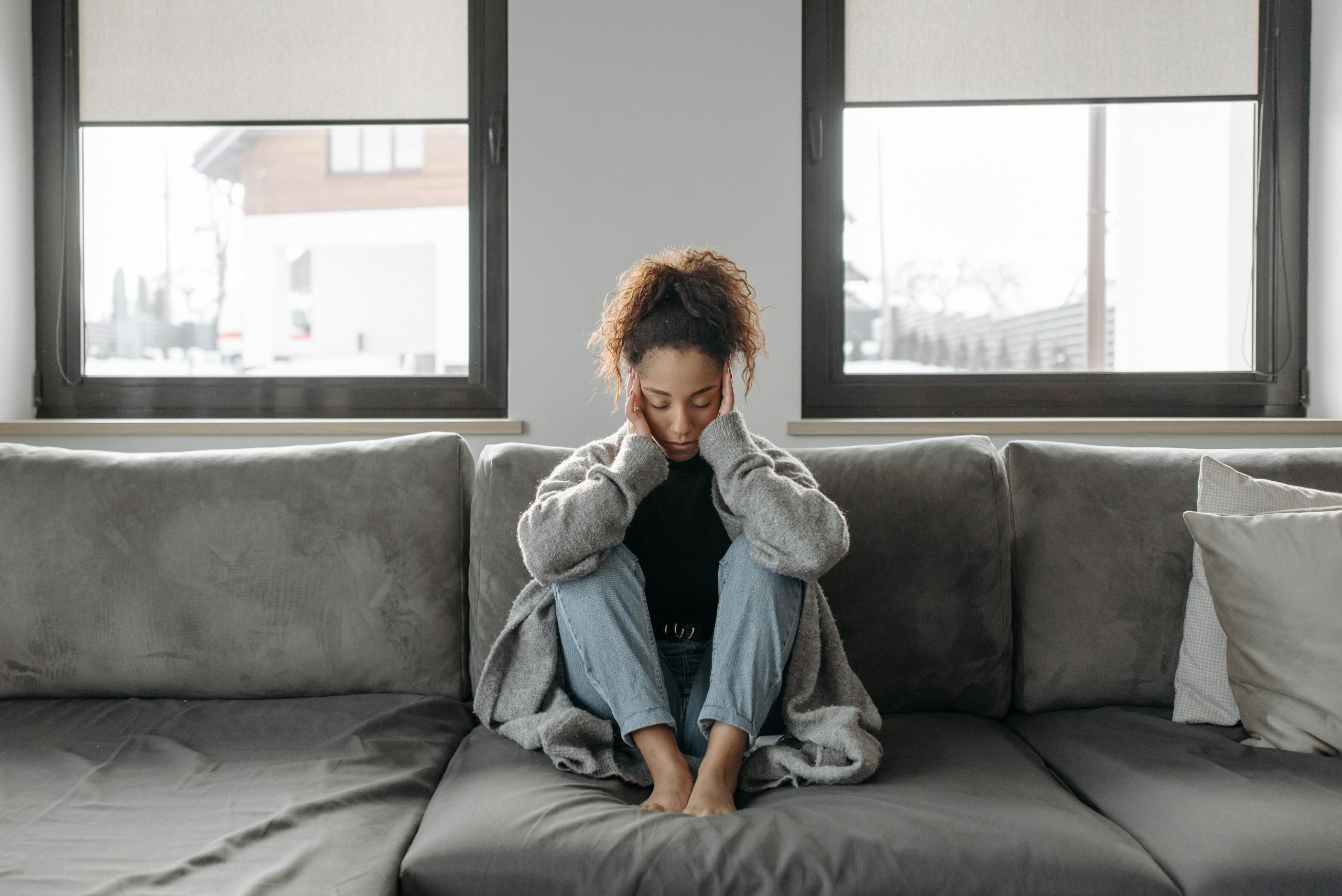 woman sitting on a couch with her hands on her temples, appearing stressed
