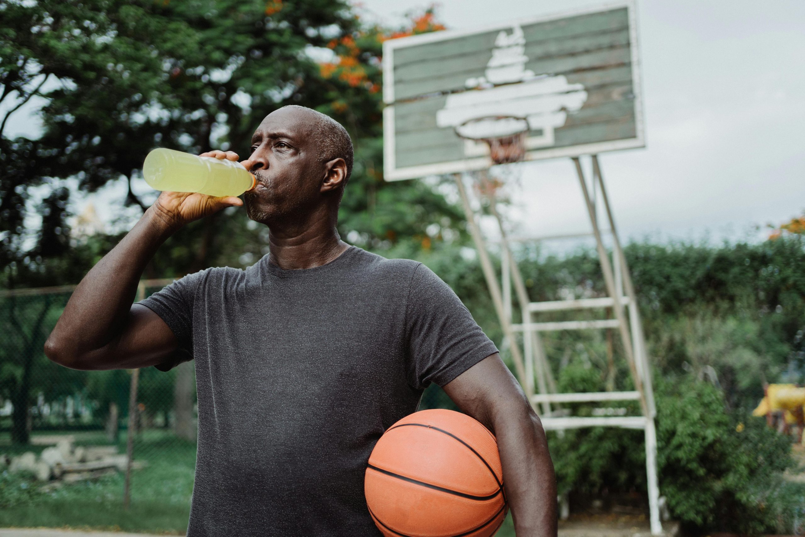 male basketball player drinking a sports drink with a ball tucked at his side between his arm and torso