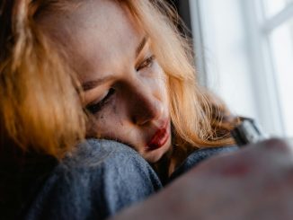 woman crying while looking out a window, with smudged eyeliner on her face