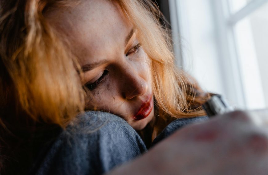 woman crying while looking out a window, with smudged eyeliner on her face