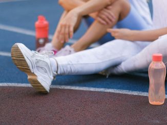 female athletes sitting on a track field, with water-filled tumblers beside them