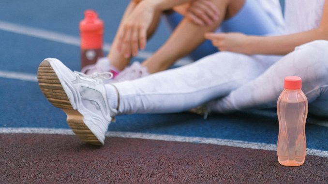 female athletes sitting on a track field, with water-filled tumblers beside them