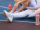 female athletes sitting on a track field, with water-filled tumblers beside them